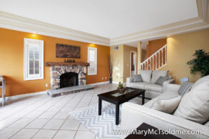 Bright living room at 2416 Vancouver Ave in North Park featuring a rustic stone fireplace with a wood mantel, golden-toned walls, and recessed lighting within tiered crown molding.