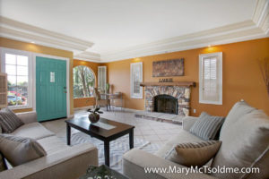 Vibrant living room at 2416 Vancouver Ave in North Park featuring a stacked-stone fireplace, a signature turquoise front door, crown molding, and a built-in office nook.