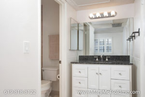 Updated bathroom at 4205 Ohio Street featuring a white vanity with a dark granite countertop, a large mirror with globe lighting, and a glimpse into the toilet and shower area.