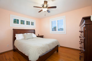 Bedroom at 3727 Suffolk Drive in Rolando Park with peach-toned walls, original hardwood floors, a dark wood sleigh bed, and windows featuring white plantation shutters.