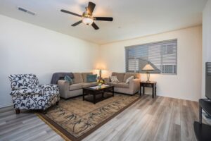 Spacious open-concept great room at 5235 Beachfront Cove Unit 102 featuring wood-style flooring, a designer ceiling fan, and custom vinyl blinds.