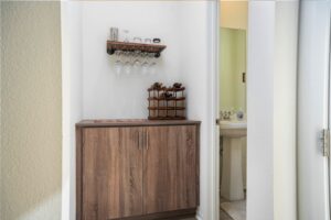 Upgraded home bar area at 5235 Beachfront Cove Unit 102 with custom wood cabinetry, wine rack, and wall-mounted glass storage located near the powder room.