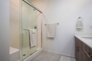 Modern primary ensuite bathroom at 5235 Beachfront Cove Unit 102 featuring a large glass-enclosed walk-in shower with white tile and a wood-finish double vanity.