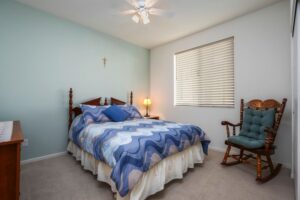 Spacious primary suite or guest room at 5235 Beachfront Cove Unit 102 featuring a ceiling fan, light blue accent wall, and an ornate wooden rocking chair.