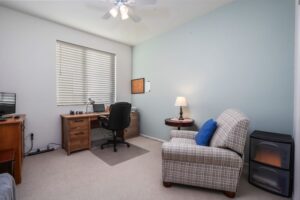 Functional home office setup in a guest bedroom at 5235 Beachfront Cove Unit 102, featuring a wooden desk, office chair, and natural light from a window with custom blinds.