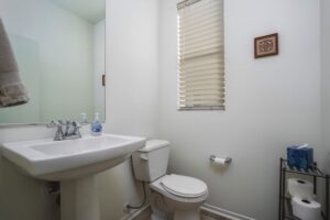 Modern powder room at 5235 Beachfront Cove Unit 102 featuring a white pedestal sink, large mirror, and custom vinyl blinds.