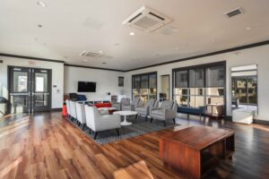 Modern community lounge at featuring hardwood floors, gray armchairs, a wall-mounted TV, and large windows.