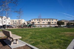Spacious grassy park area and community playground near 5235 Beachfront Cove Unit 102, featuring park benches, a paved walking path, and surrounding residential townhouses.
