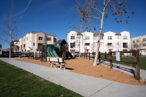 Wide view of the neighborhood park and playground at 5235 Beachfront Cove Unit 102, showing modern multi-story townhomes, a paved walking path, and green lawn areas.