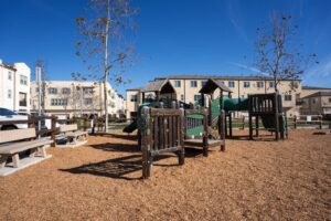 Outdoor children's playground with green slides, climbing structures, and wood chip ground cover, located near the townhomes at 5235 Beachfront Cove Unit 102