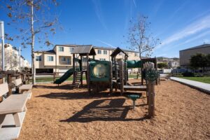 Outdoor children's playground with green slides, climbing structures, and wood chip ground cover, located near the townhomes at 5235 Beachfront Cove Unit 102