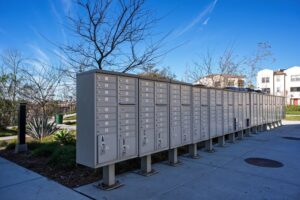 Community cluster mailboxes on a paved walkway near 5235 Beachfront Cove Unit 102, featuring secure metal units under a clear blue sky.