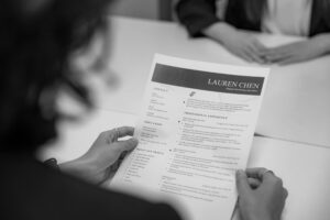 Eine Person im HR-Bereich analysiert aufmerksam einen ausgedruckten Lebenslauf; symbolisiert die menschliche Urteilskraft gegenüber automatisierten KI-Rankings.