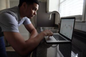 African American man in a grey shirt hunched over a laptop.