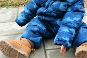 Baby in snowsuit sitting on interlocked patio with grass in the background