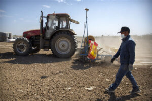 A worker walks next to a tractor during planting of a cotton field in China. - Photo: AP Photo/Mark Schiefelbein