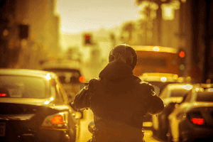 Motorcyclist driving through heavy traffic while the sun sets. 