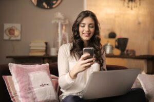 Woman looking at phone in front of laptop