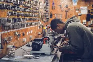 A focused craftsman works in a key-making workshop surrounded by tools and equipment.