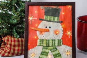 Decorate your home for the holiday season with this easy-to-make Lighted Snowman Picture. It’s fun to put together and perfect for hanging up around the home to get into the holiday spirit. This DIY Christmas craft is made with a gift bag and a dollar store frame. It is a fun dollar store Christmas craft.