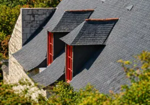 Steep slate-grey roof with dormers, comparing metal and asphalt roofing costs