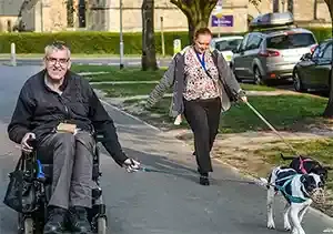 Man in wheelchair enjoying a walk with his caregiver and dog, highlighting independence and companionship through home care support.