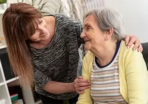 Caregiver offering reassurance and companionship to an elderly woman at home, reflecting compassionate home care support.
