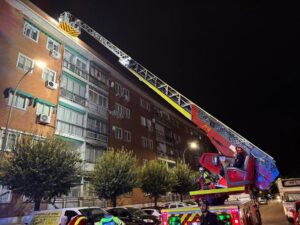 Bomberos en una camioneta con escalera extensible frente a un edificio en Madrid, trabajando en la noche tras las tormentas.