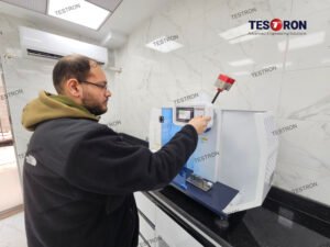 Operator using TT-IZ-5.5 Izod Impact Tester by Testron for plastic impact strength testing in quality control laboratory