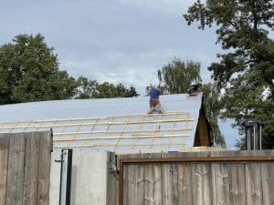 Dacharbeiten auf einem Holzhaus bei Wellnesshof RaJa, Handwerker installieren eine nachhaltige Dachdeckung in einer natürlichen Umgebung. Hochwertige Bauarbeiten für nachhaltigen Wellness- und Erholungsurlaub.