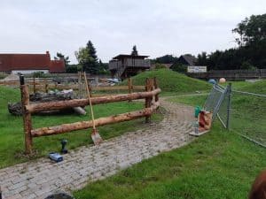 Natursteinweg, Holzsichtschutz, Gartenarbeit, Bauarbeiten, grüner Rasen, Werkzeuge, Blumen, ländliche Umgebung, Gartenzaun, Natur, Wellnesshof RaJa, Erholung in der Natur, ländliche Atmosphäre, Gartengestaltung, entspannende Naturkulisse.