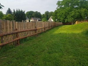 Naturgarten mit grünem Rasen, Holzzaun und Bäumen, ländliche Umgebung, entspannte Atmosphäre, Fokus auf Natur und Erholung, ideal für Wellness und Rückzugsorte.