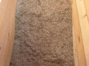 Nahaufnahme einer braunen Naturfaserdämmmatte, eingerahmt von zwei Holzbalken