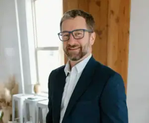 blake ingram wearing a white button down shirt and a navy blue blazer with his hands in his pockets