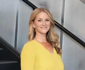 lindsay davis standing on a staircase, holding a folder, wearing a yellow sweater