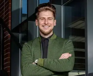 Michael Abernathy smiling while crossing his arms, wearing a black shirt with a green blazer on top