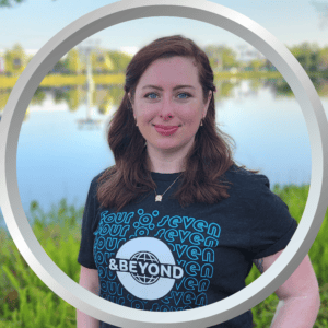 Relaxed woman wearing "407 and Beyond" t-shirt near a lake with boats and trees.