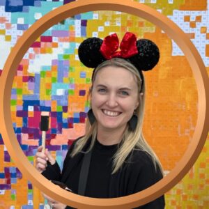 Bright smiling woman wearing Minnie Mouse ears at a colorful pixel art mural, showcasing creative vacation photo ideas.