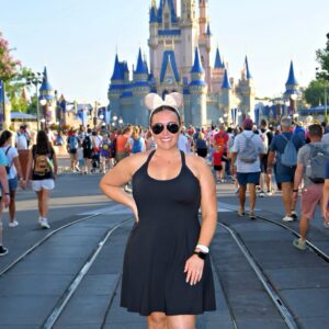 Colorful Disney castle at Magic Kingdom with smiling woman in black dress and Minnie Mouse ears.