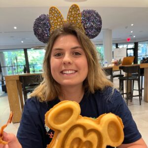 Cute woman wearing Minnie Mouse ears headband and holding a Mickey Mouse waffle at 407 Vacations.