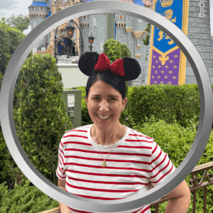 Smiling woman with Minnie Mouse ears at Disney theme park with castle backdrop.