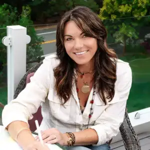 nicole flamer wearing a white button down shirt, colorful jewelery holding a pen and writing on a pad