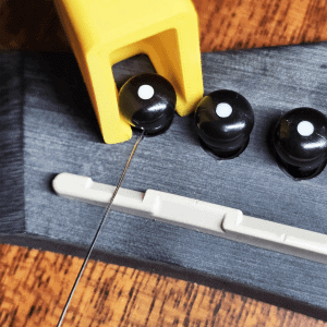 Guitar string winder in yellow removing bridge pins from acoustic guitar
