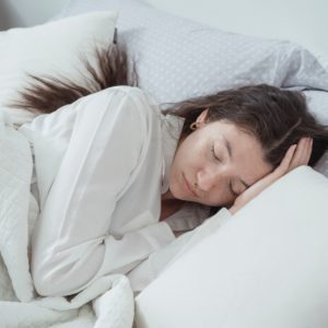 A woman dressed in white sleeping in a bed with white bedding showcasing the best comforter for hot sleepers.