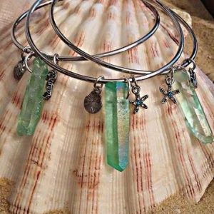 Mermaid Tail Bracelet, collection of shiny silver bangles with green crystal pendants and starfish charms displayed on a seashell.