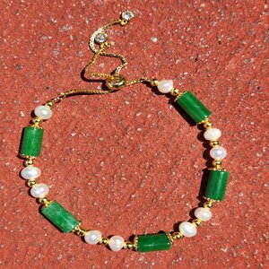 Jade and Pearl Bracelet, a gold chain jewelry piece featuring green jade beads and white pearls, displayed on a red textured surface.