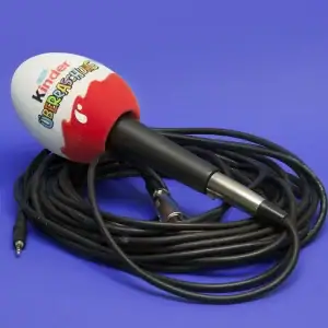 Handheld microphone with a custom printed foam windscreen (logo and colours) on a blue background, shown with a coiled cable for broadcast and interview use.