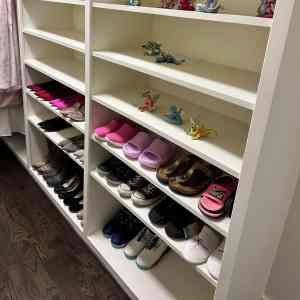 Colorful children's shoes and toy figurines on white shelving unit, organized shoe rack for kids' footwear, ideal for home living spaces, emphasizing neatness and playful decor, suitable for family-friendly environments.
