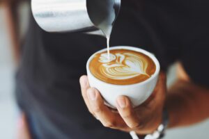 pexels photo 302899 302899 1 Close-up of a barista pouring milk to create latte art in a coffee cup.