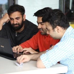 Three men sitting at a table, smiling and looking at a laptop screen together.